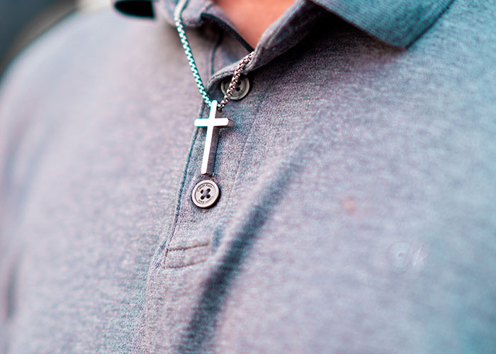 A close-up of a silver cross necklace worn by a man, potentially reflecting a spiritual aspect of a cringe midlife crisis.