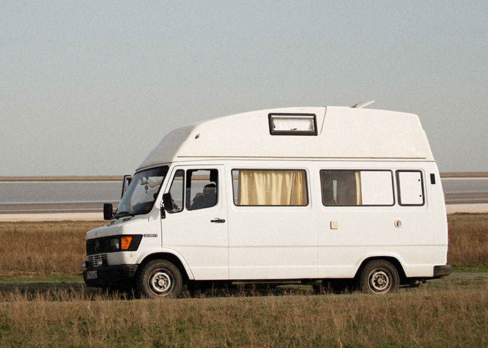 A white camper van parked in a field, symbolizing a potential cringe midlife crisis.