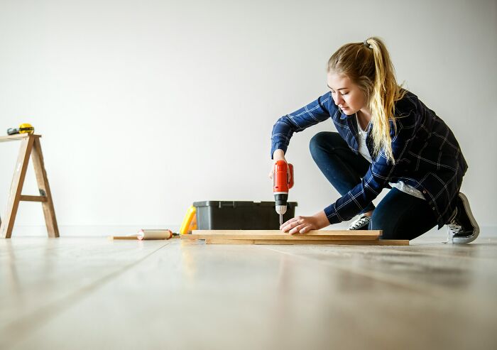 A woman using a drill on wood, showcasing a poverty habit of DIY that helps save money.