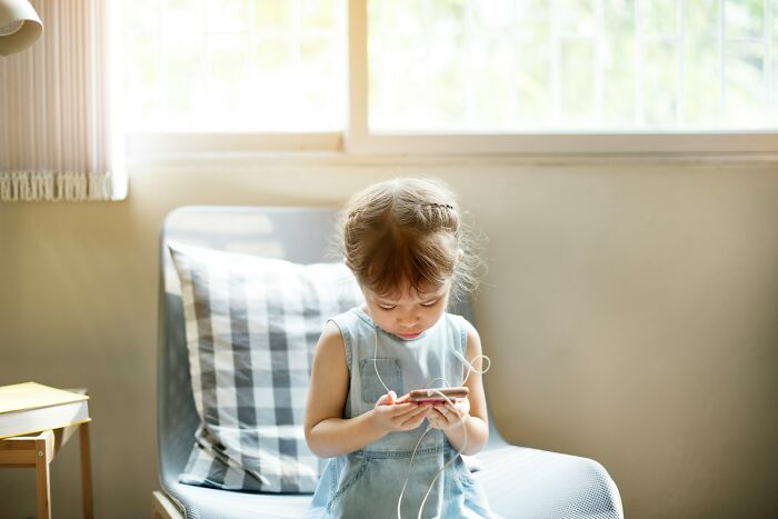 Little girl engrossed in a smartphone, depicting potential signs of a horrible parent.