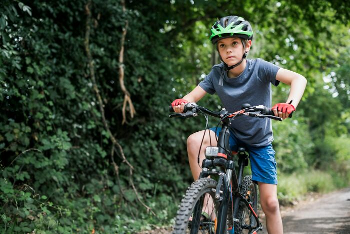A young boy in a helmet and gloves on a mountain bike, looking determined, representing a horrible parent scenario.