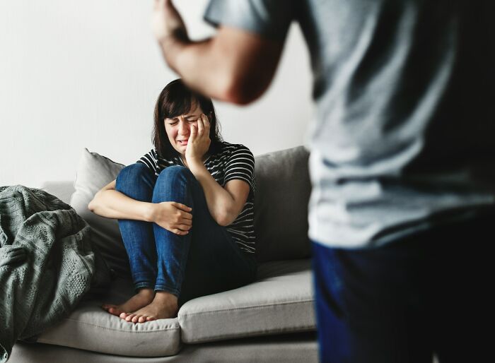A crying woman on a couch as a man stands over her, highlighting interesting neighbors.