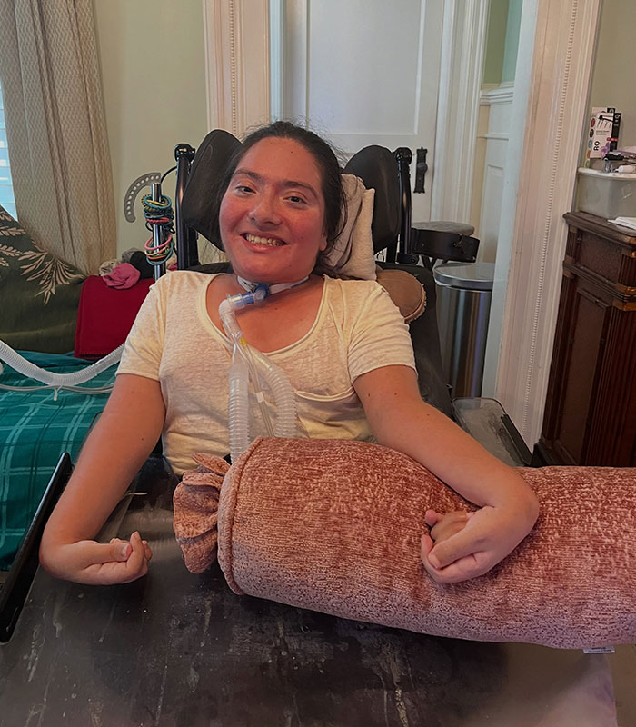A disabled customer in her home, seated in a wheelchair, smiling at the camera, after receiving the offensive birthday message.