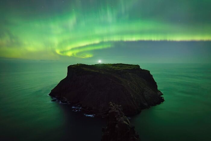 A breathtaking astrophotography image from David Malin Awards, featuring the green aurora borealis over a dark island.