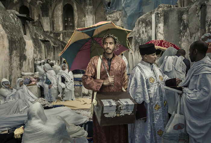 A man holding a colorful umbrella and a box, standing in a crowded, historic setting, highlighting unique street photography.