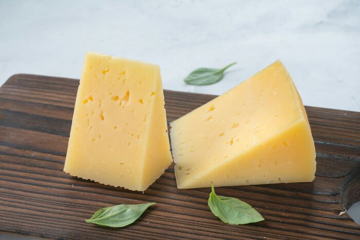 Two triangular pieces of cheese with basil leaves on a wooden cutting board, exemplifying questionable Instacart shopper choices.
