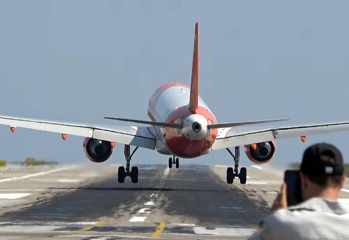A person photographing a plane on the runway, highlighting the potential danger of a jet engine blast.