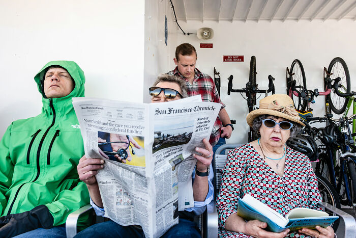 Three people sitting on a bench, one reading a newspaper, in a street photography award scene.