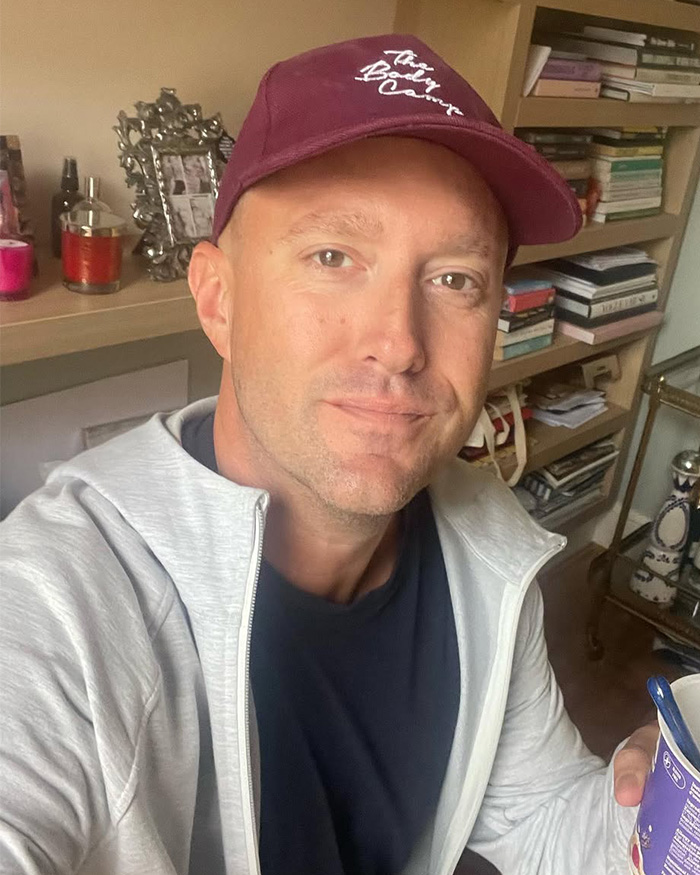 Singer James Blunt in a maroon cap, light grey hoodie, and dark shirt, looking directly at the camera. He is sitting in a room with shelves of books and decorative items. Singer James Blunt in a maroon cap, light grey hoodie, and dark shirt, looking directly at the camera. He is sitting in a room with shelves of books and decorative items.