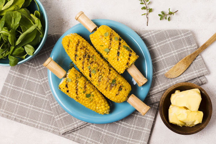 Grilled corn on the cob on a blue plate, highlighting unhinged house rules that make sense to the family.