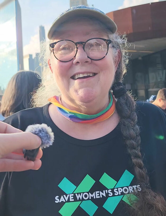 Smiling woman in glasses wearing a SAVE WOMEN'S SPORTS shirt, interviewed about anti-trans protesters WNBA question. Smiling woman in glasses wearing a SAVE WOMEN'S SPORTS shirt, interviewed about anti-trans protesters WNBA question.
