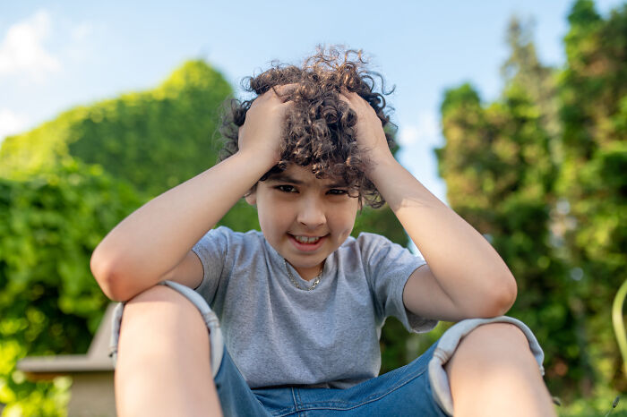 A young boy with curly hair, hands on his head, smiling at the camera, a sign from the universe.