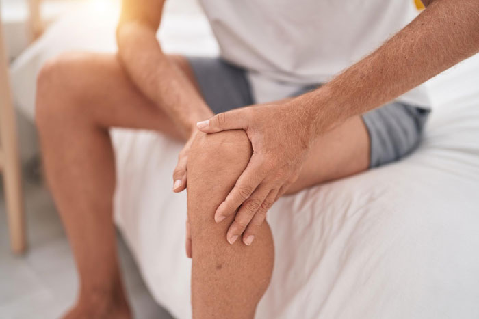 A person holding their knee, experiencing joint pain and disability. The image highlights the struggle with a disability.