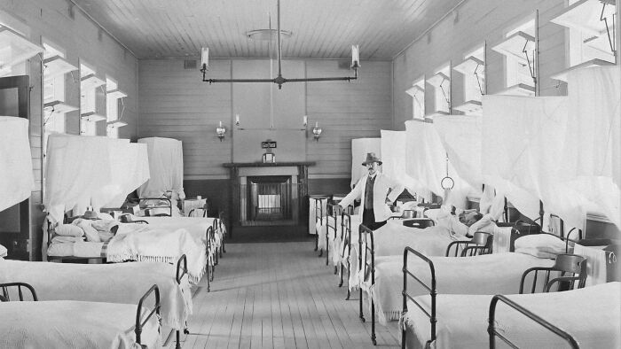 A nurse in a historical hospital ward with many beds, showcasing past medical treatment methods and tools.