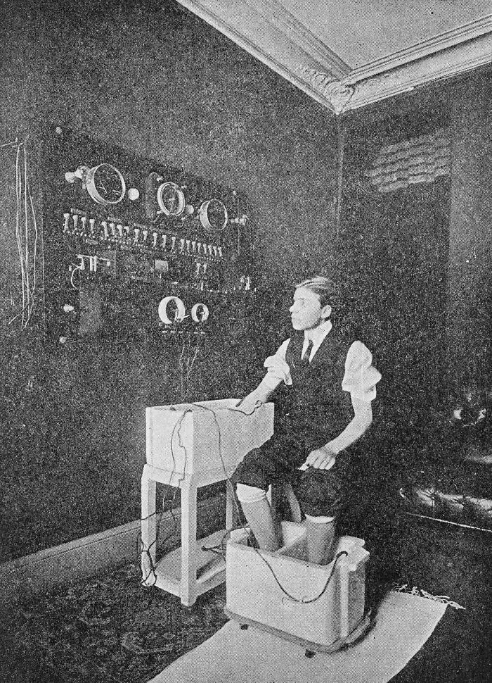 A patient receiving terrifying medical treatment with foot and hand baths connected to a large electrical panel on the wall.