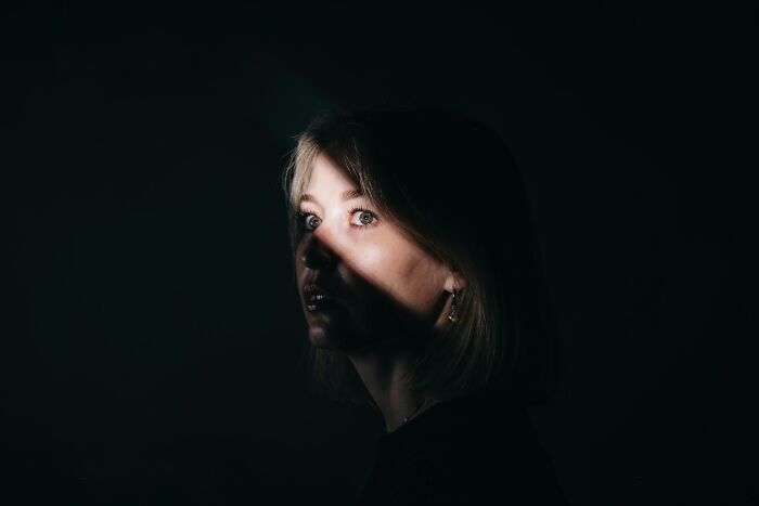 A woman with scared eyes, lit by a single beam, pondering creepy true stories that question reality.