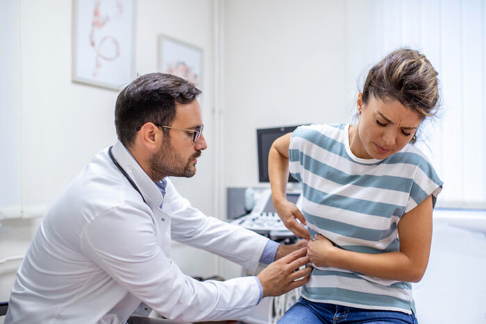A female patient holds her stomach in pain as a doctor examines her during a consultation. Patients.