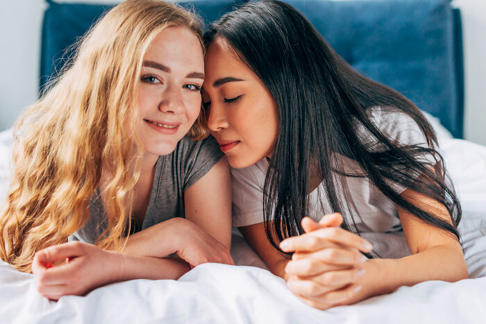 Two happy female patients lying close on a bed, smiling, representing patient comfort.