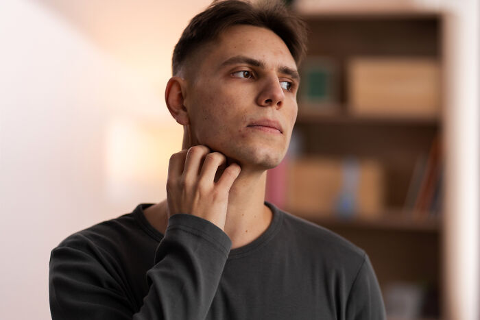 A young male patient scratching his neck, looking concerned or thoughtful, reflecting common patient complaints to doctors.