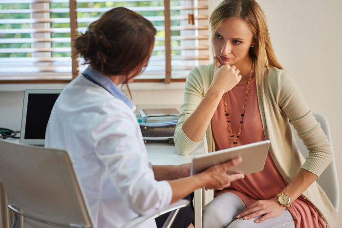 Female patient looking intently at a doctor, who is holding a digital tablet during a consultation.