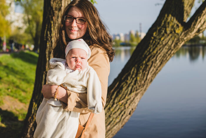 A mother holds her baby outdoors near a tree and water, reflecting on silly things patients have said to doctors.