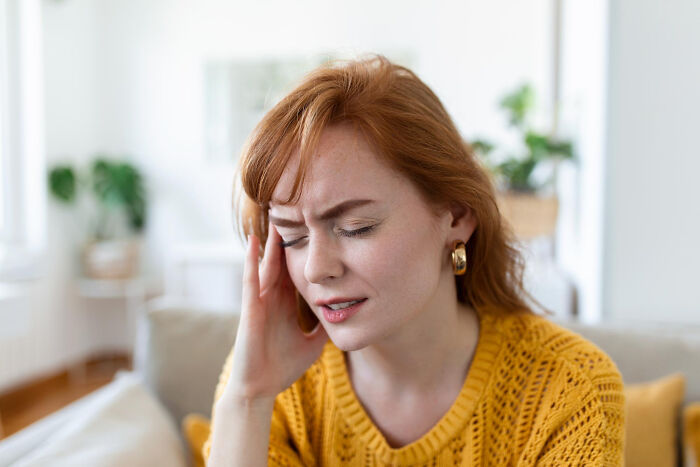 A woman with red hair clutches her head in pain, representing a patient who said something stupid to doctors.
