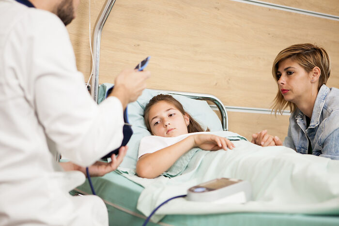 A doctor checks a young patient's blood pressure in a hospital bed, with her mother looking on. Patients.