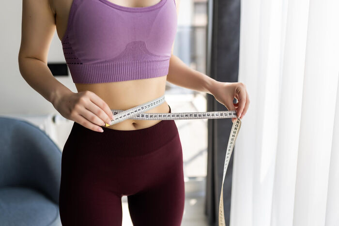 A woman in athletic wear measures her waist with a tape measure. Patients.
