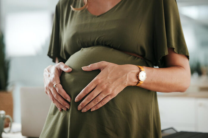 A pregnant woman in a green dress gently holds her belly with both hands. Patients.