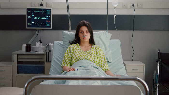 A young female patient lies in a hospital bed with an IV drip and heart monitor in the background. Patients.