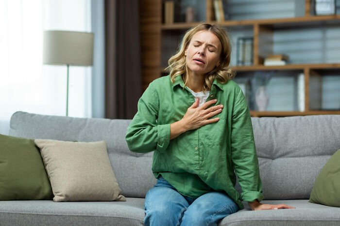 A female patient on a sofa experiencing chest pain, holding her hand to her chest, a serious concern patients report to doctors.