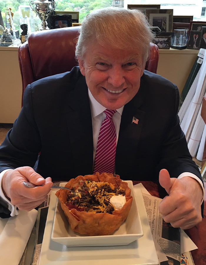 Smiling Donald Trump gives a thumbs up while holding a fork over a taco bowl, highlighting his health marker. Smiling Donald Trump gives a thumbs up while holding a fork over a taco bowl, highlighting his health marker.