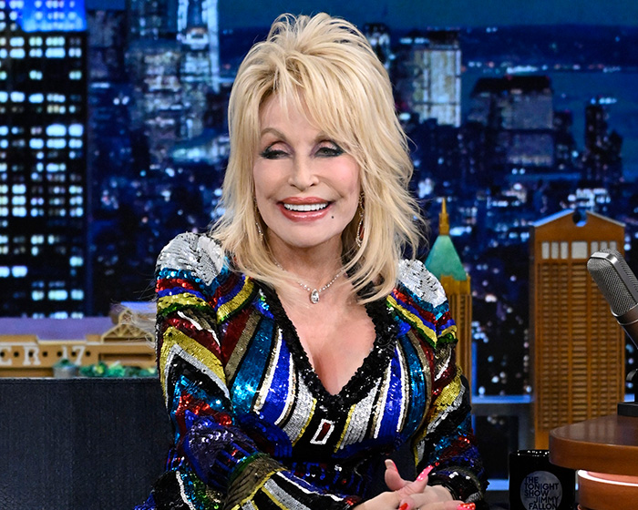 Dolly Parton in a sequined jacket, smiling brightly, showcasing her grace amid feuds and controversies.