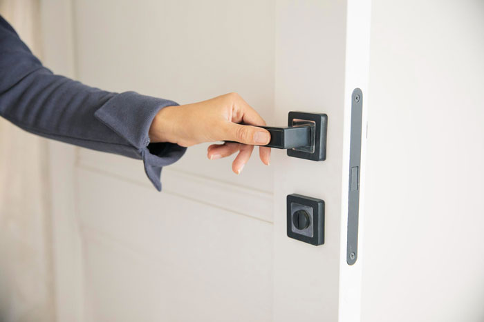 A woman's hand reaches for a modern black door handle, illustrating the issue of a controlling mom forbidding a daughter from locking her door. A woman's hand reaches for a modern black door handle, illustrating the issue of a controlling mom forbidding a daughter from locking her door.