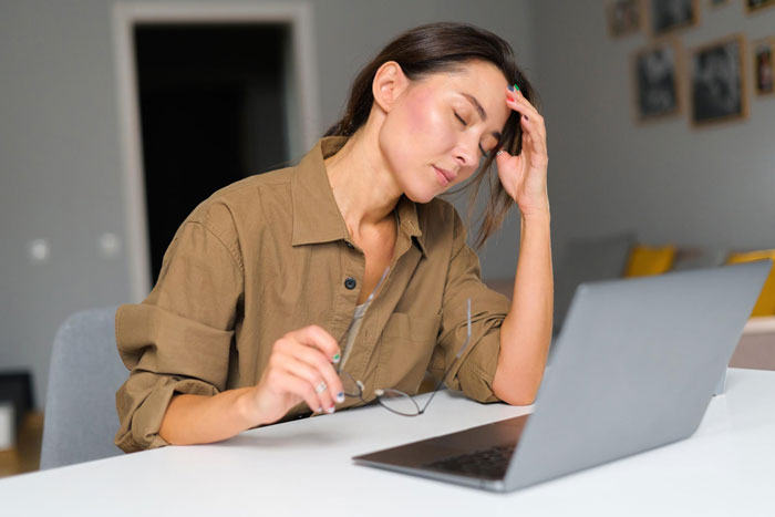 A distressed 22YO daughter, head in hand, in front of a laptop, struggling with her controlling mom. A distressed 22YO daughter, head in hand, in front of a laptop, struggling with her controlling mom.