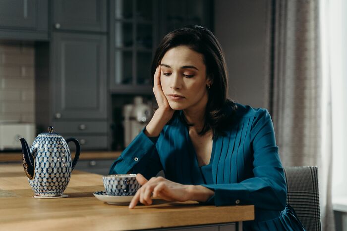 A conventionally attractive woman looking thoughtful while holding a teacup.