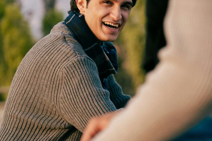 A smiling man looks over his shoulder, engaging in a conversation about being conventionally attractive.