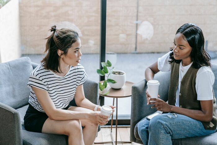 Two women conversing and holding coffee cups, discussing perceptions of being conventionally attractive.