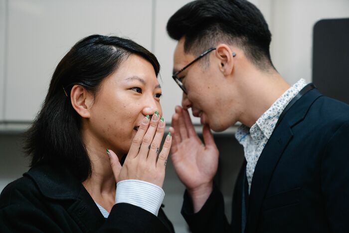 A man whispering to a woman, sharing secrets about societal views on being conventionally attractive.