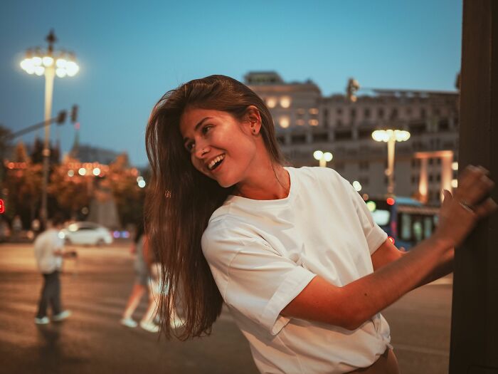 A conventionally attractive woman smiling and looking over her shoulder at dusk.