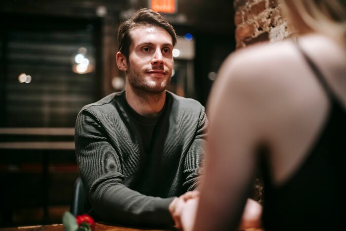 A man looking attentively at a woman across the table, considering what it means to be conventionally attractive.