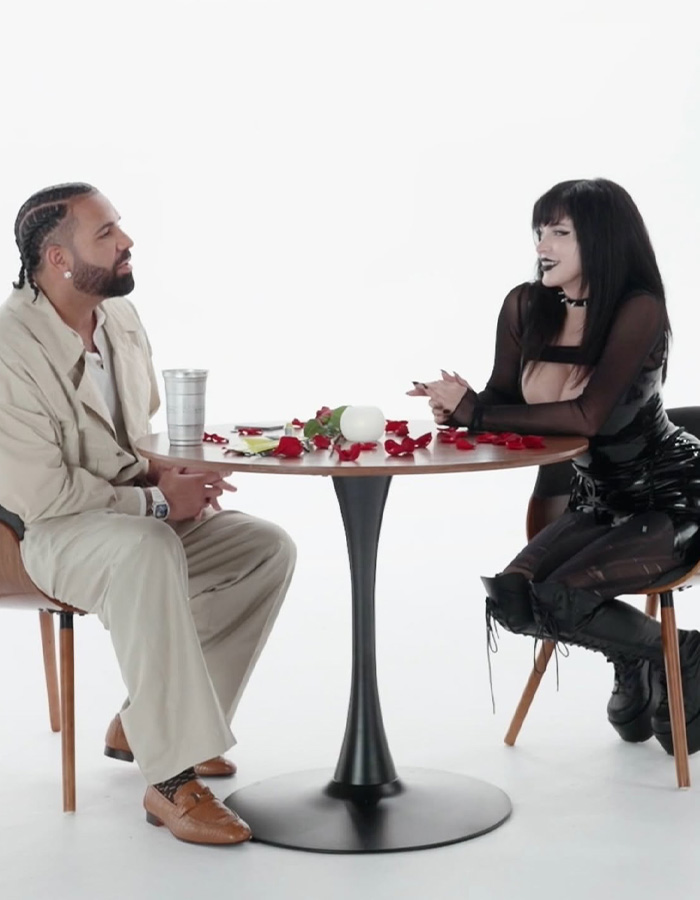 Drake and Goth Baddie on a dating show, seated at a table with rose petals. Drake and Goth Baddie on a dating show, seated at a table with rose petals.