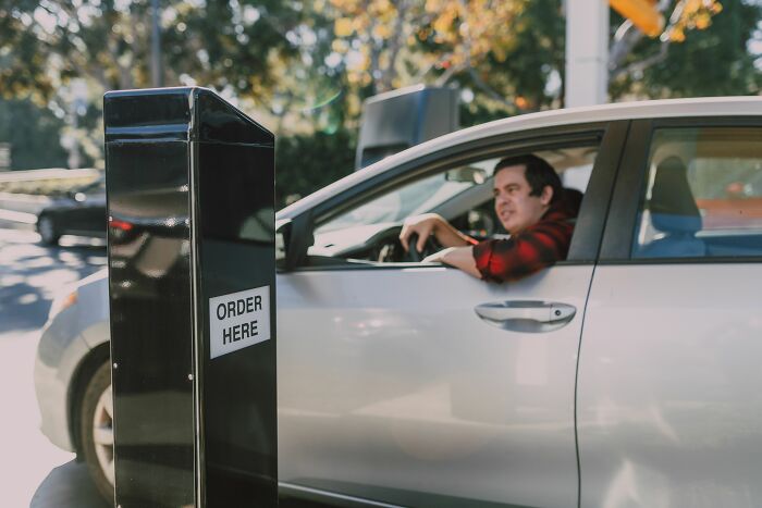 A man in a car at a drive-through speaker, contemplating crazy things customers said.