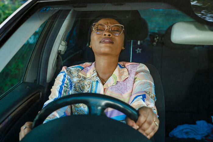 A woman in a car with eyes closed, thinking about crazy things customers said at a drive-through.