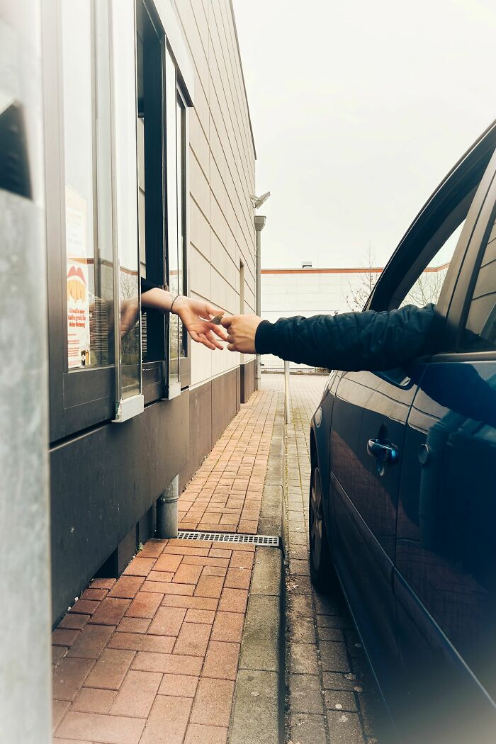 A customer reaching out from a car window to an employee at a drive-through, illustrating a typical customer interaction.