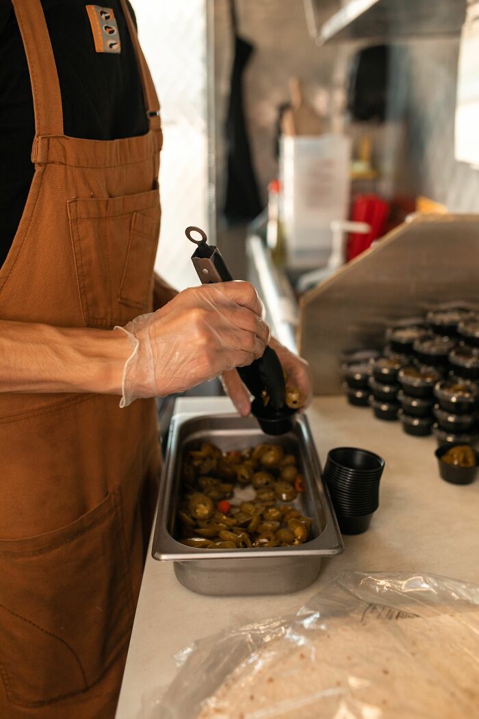 An employee in an apron and gloves preparing food at a drive-through, showing behind-the-scenes work.