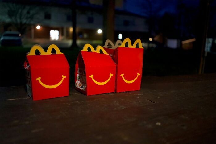 Three Happy Meal boxes on a wooden table at night, representing typical drive-through customer orders.