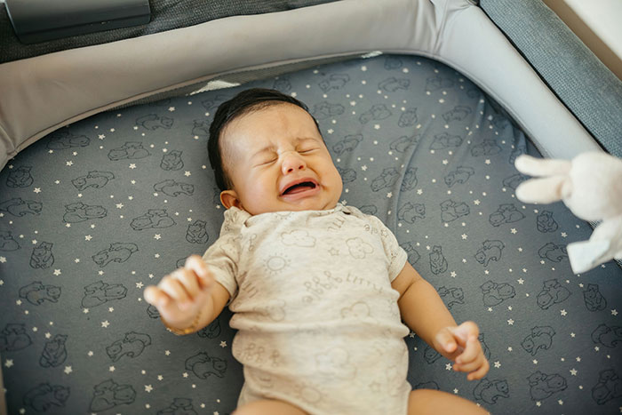 An infant crying baby lying in a crib, illustrating the issue of parents gaslighting the babysitter. An infant crying baby lying in a crib, illustrating the issue of parents gaslighting the babysitter.
