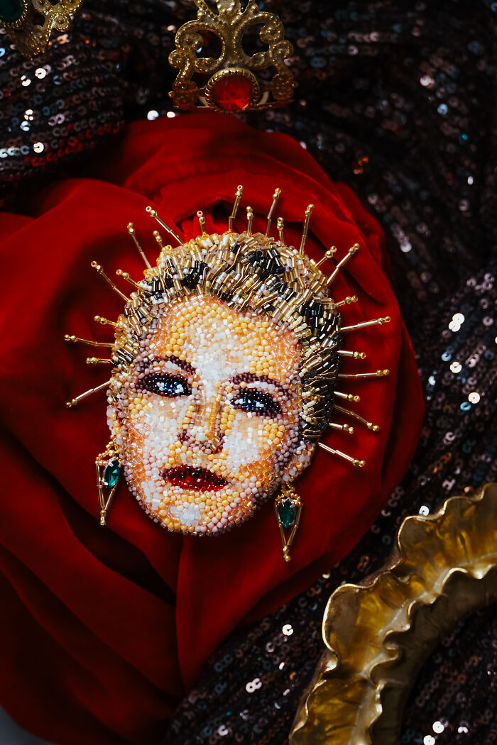 An intricate beaded creation by Tiffany Pisani on a red velvet background, featuring a woman's face adorned with a golden crown.