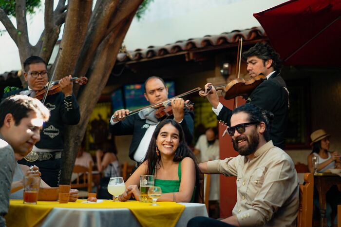 Tourists enjoying mariachi music and drinks outdoors, reminded to be respectful when they visit other countries.